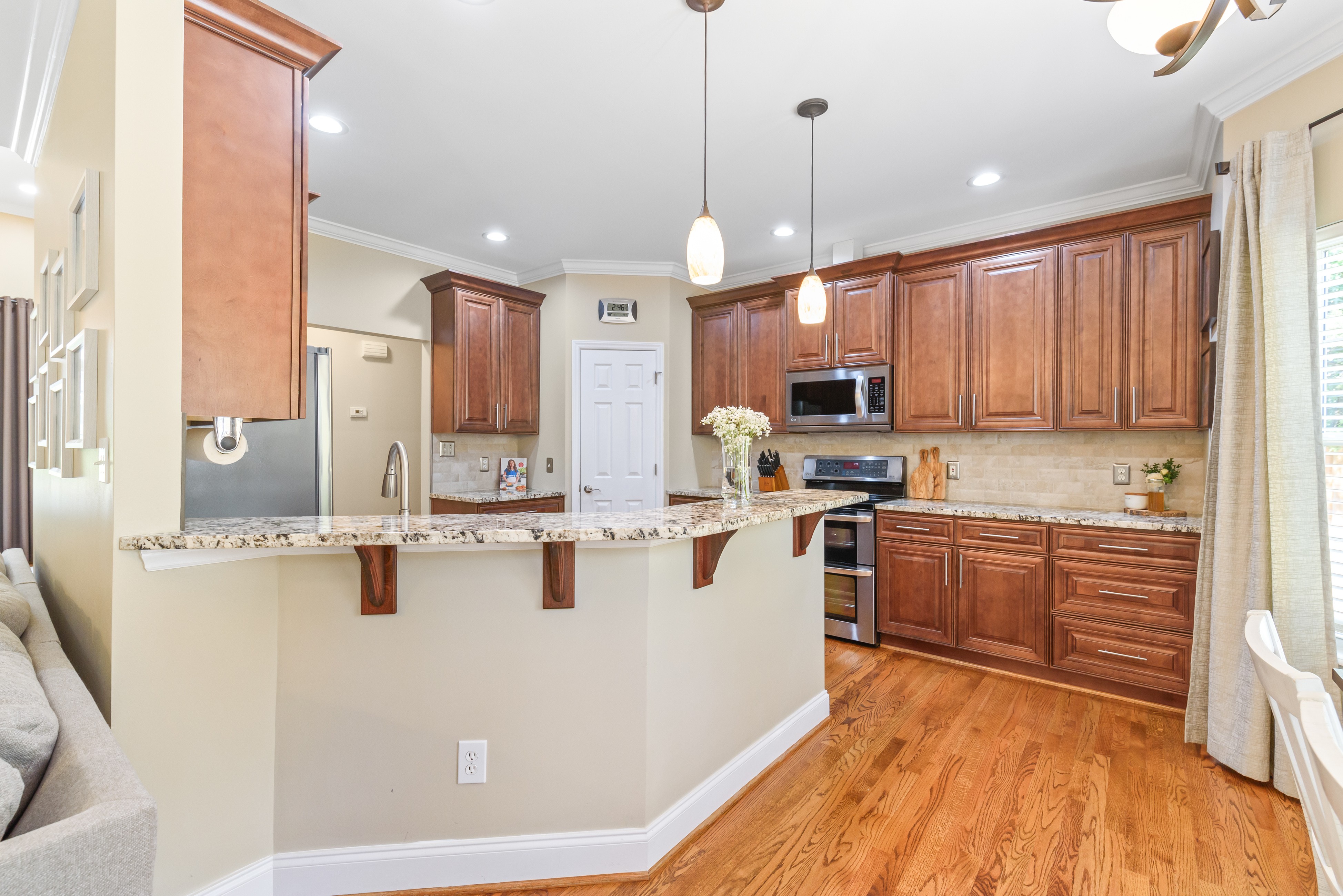 Kitchen with granite breakfast bar, pendant lighting, wood cabinetry, pantry door, and stainless appliances