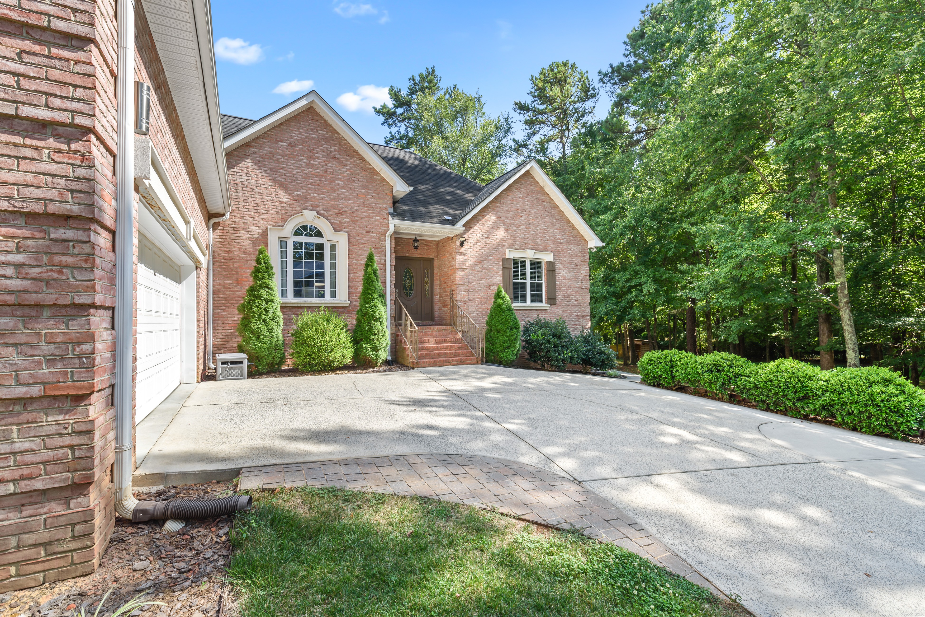 Close view of front entry—arched window, brick steps with railings, shrubs, and driveway beside garage