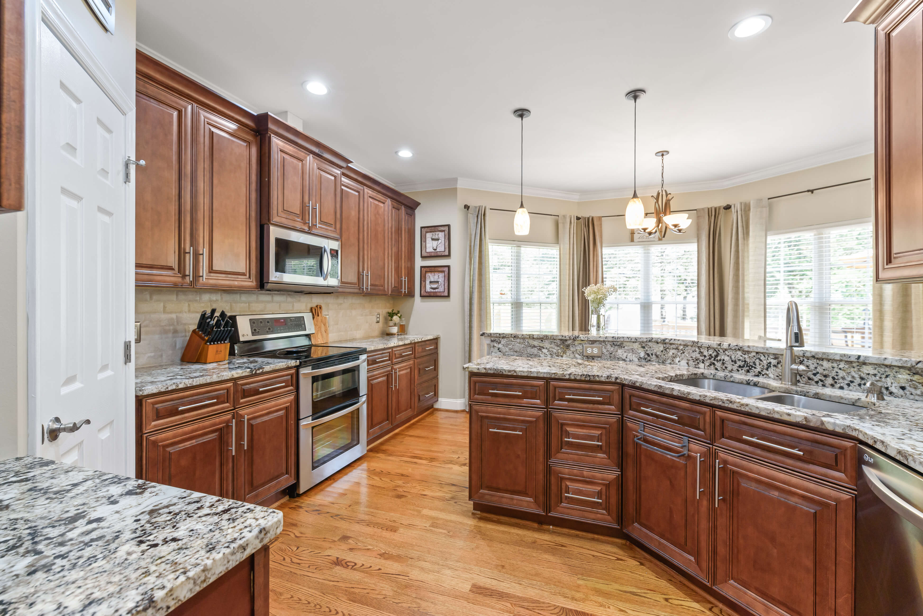 Wide kitchen with curved sink peninsula, pendant lights, granite surfaces, and windows over the breakfast area