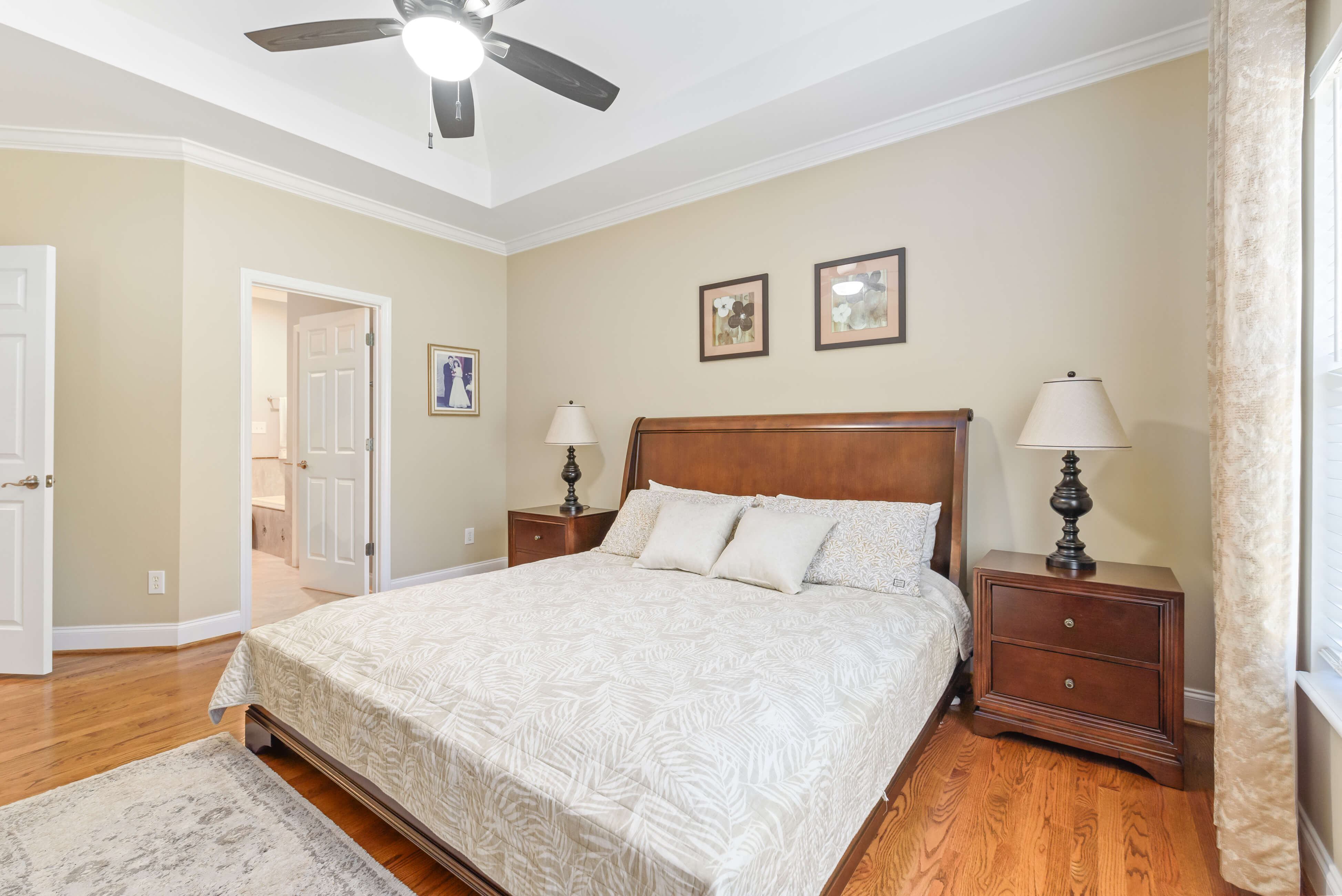 Primary bedroom facing ensuite entry with tray ceiling, nightstands, and ceiling fan