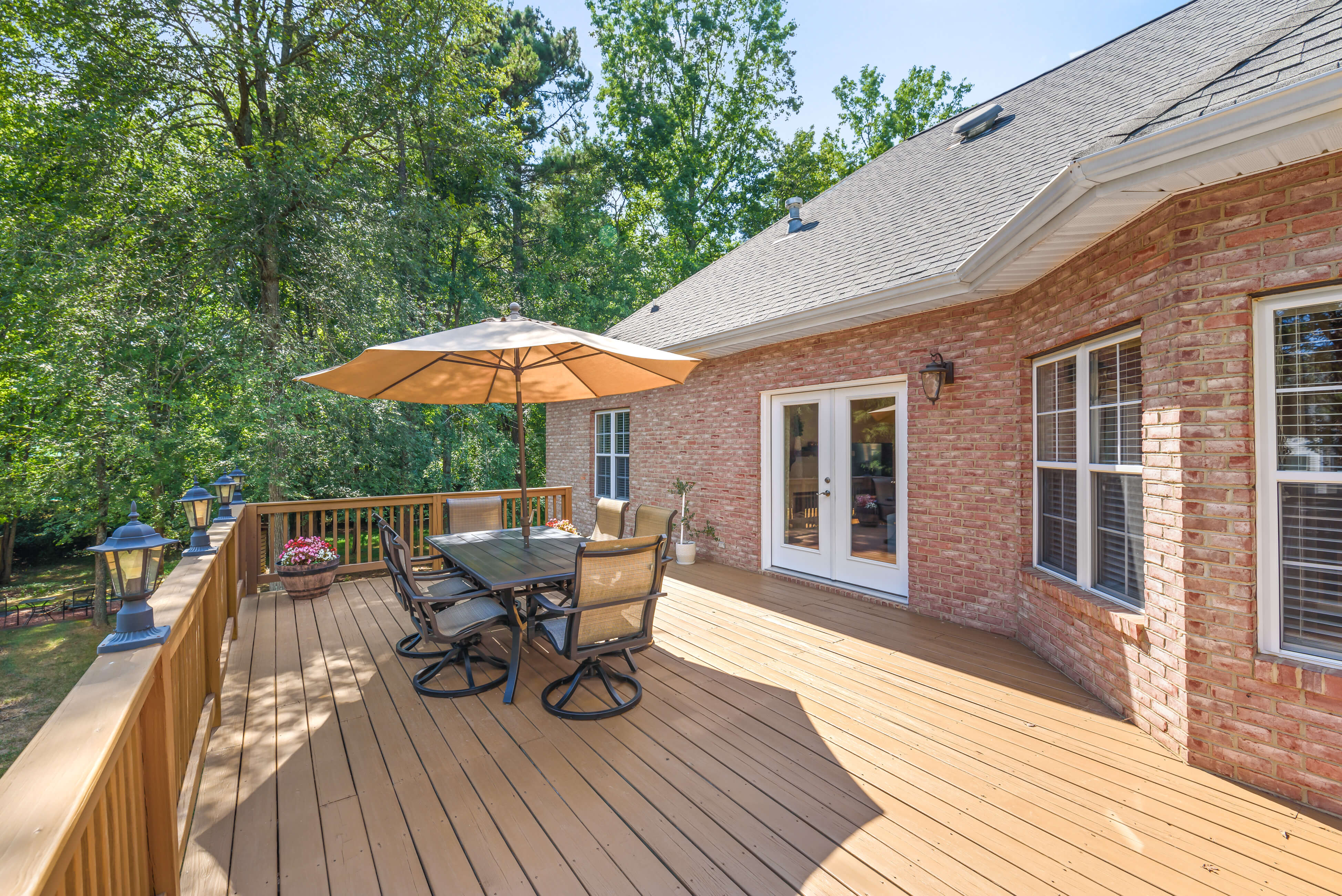 Brick exterior with French doors opening to a large deck featuring railing lights and an umbrella dining set.