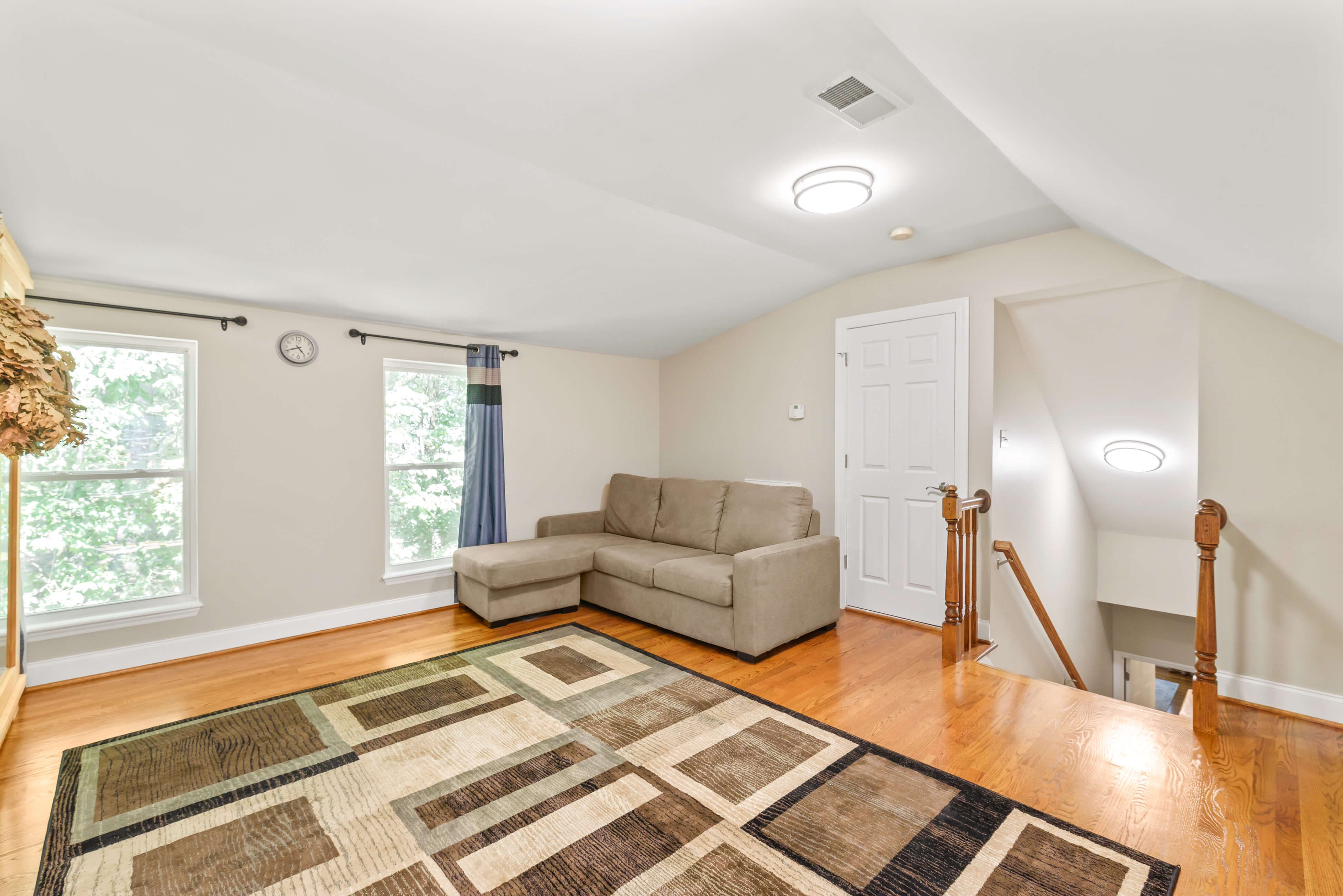 Bonus room with sectional sofa, two windows, area rug, and stair landing