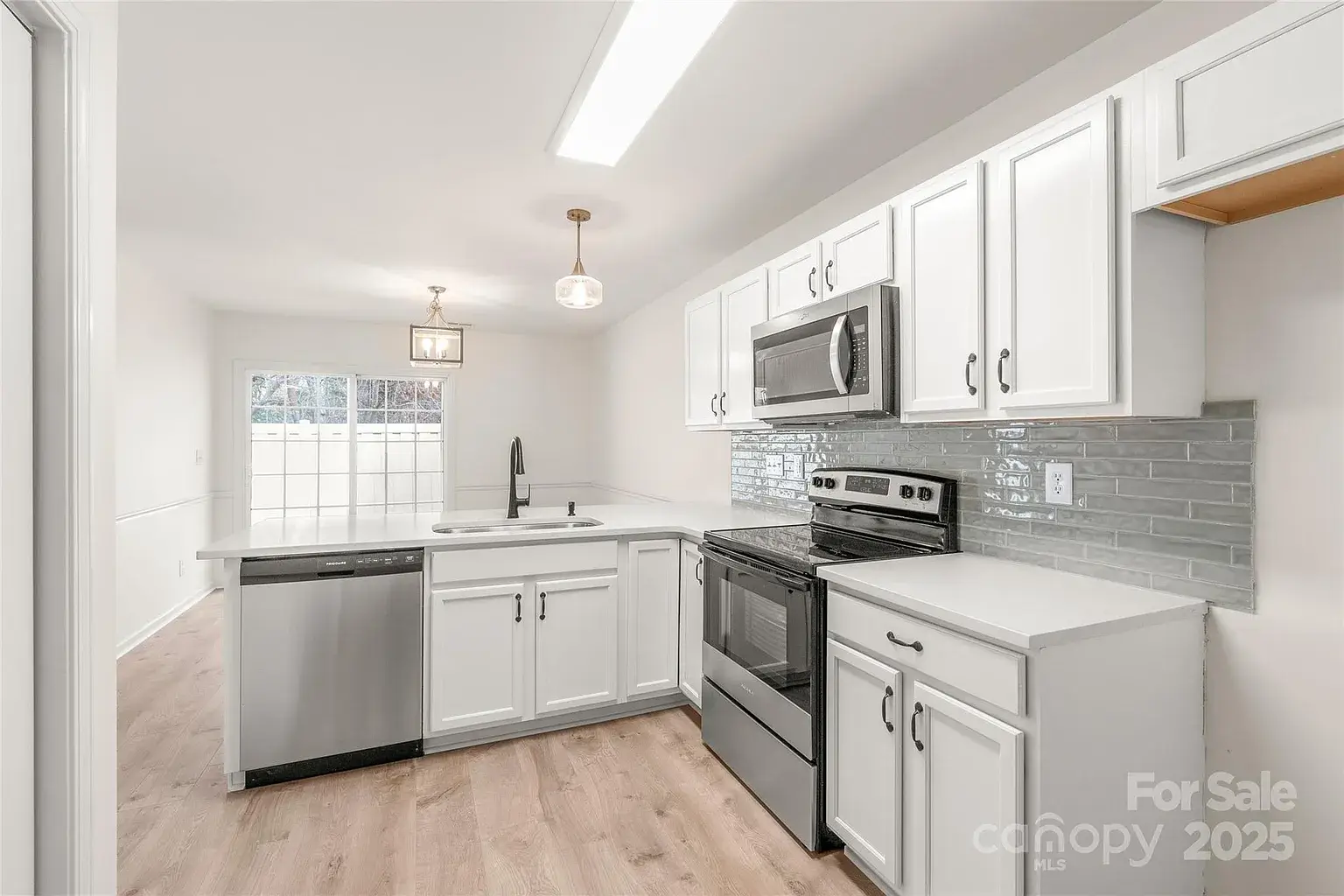 Updated white kitchen with stainless steel appliances, gray subway tile backsplash, peninsula sink, and view toward dining area.