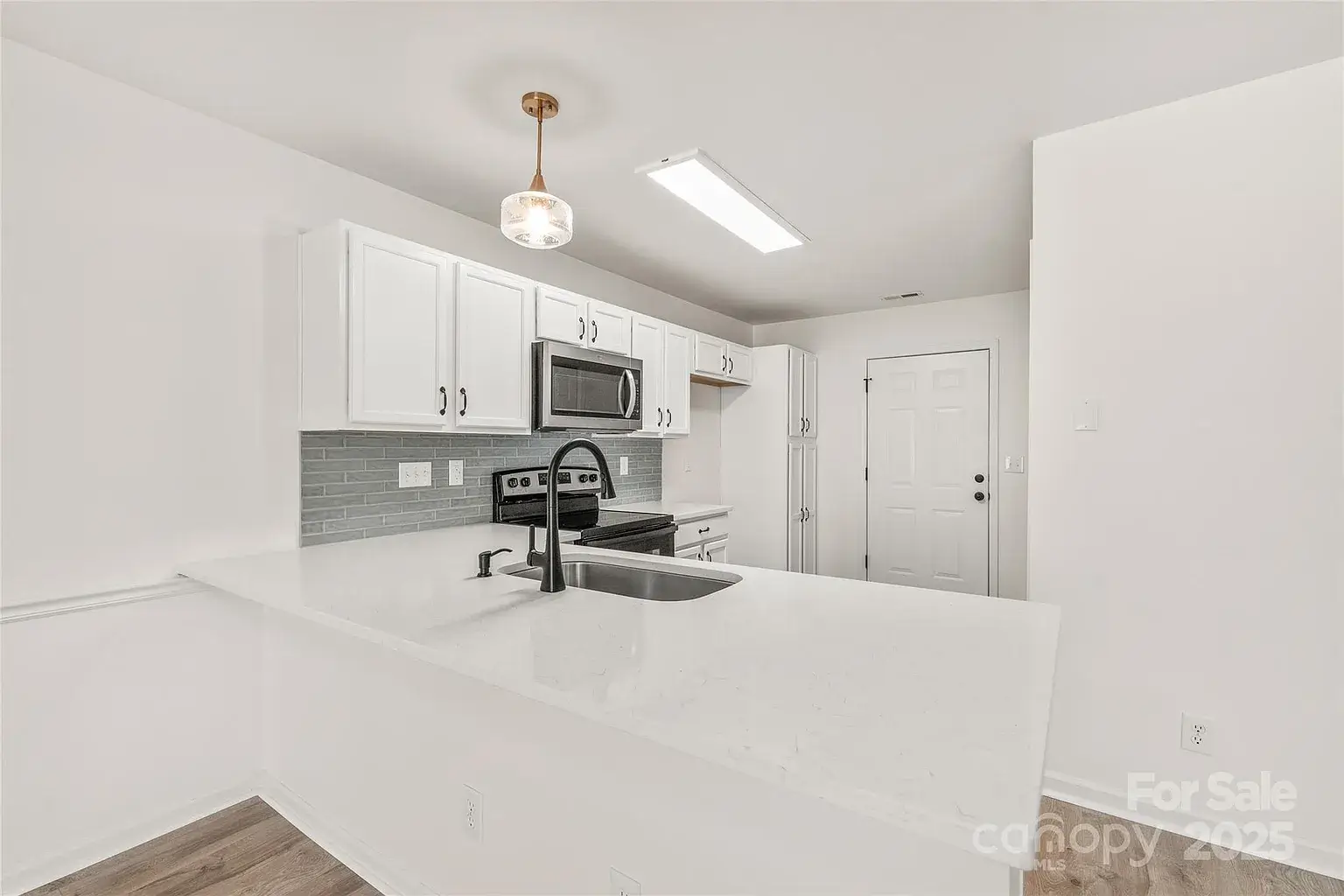 Updated kitchen with white cabinets, quartz breakfast bar, stainless steel appliances, gray tile backsplash, and modern pendant lighting.