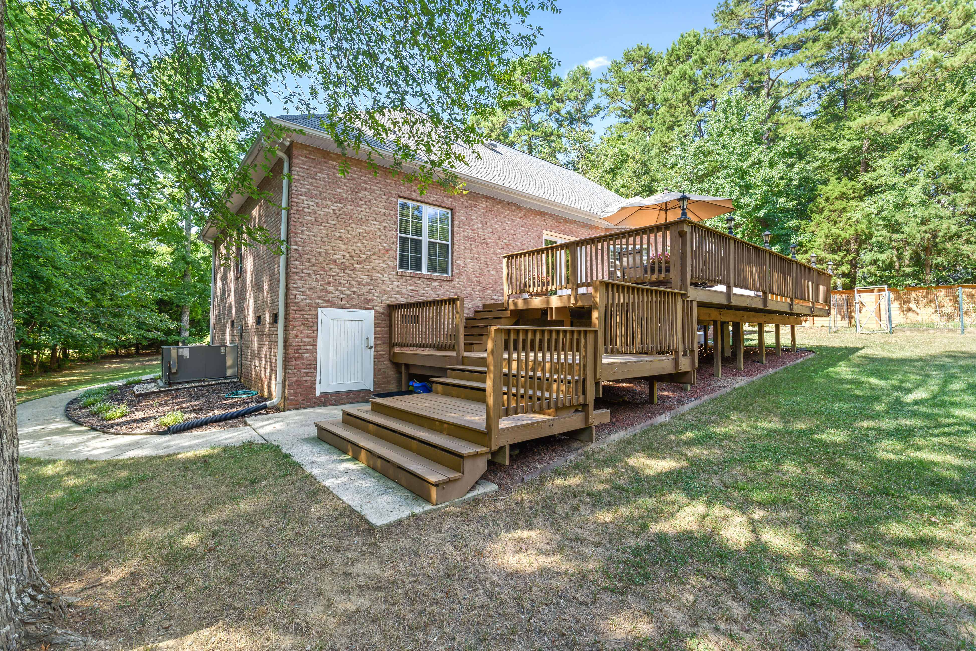 Side view of elevated deck with multiple staircases, small storage door, and fenced backyard with trees.