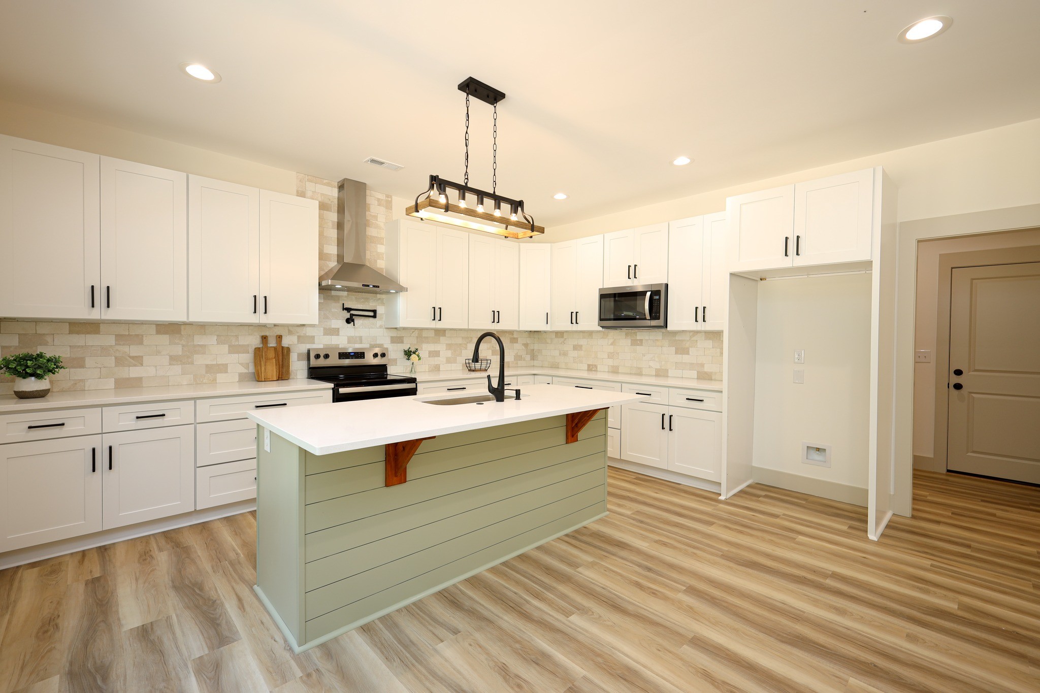Modern kitchen with white cabinets, stainless steel appliances, tile backsplash, and center island with farmhouse-style paneling.