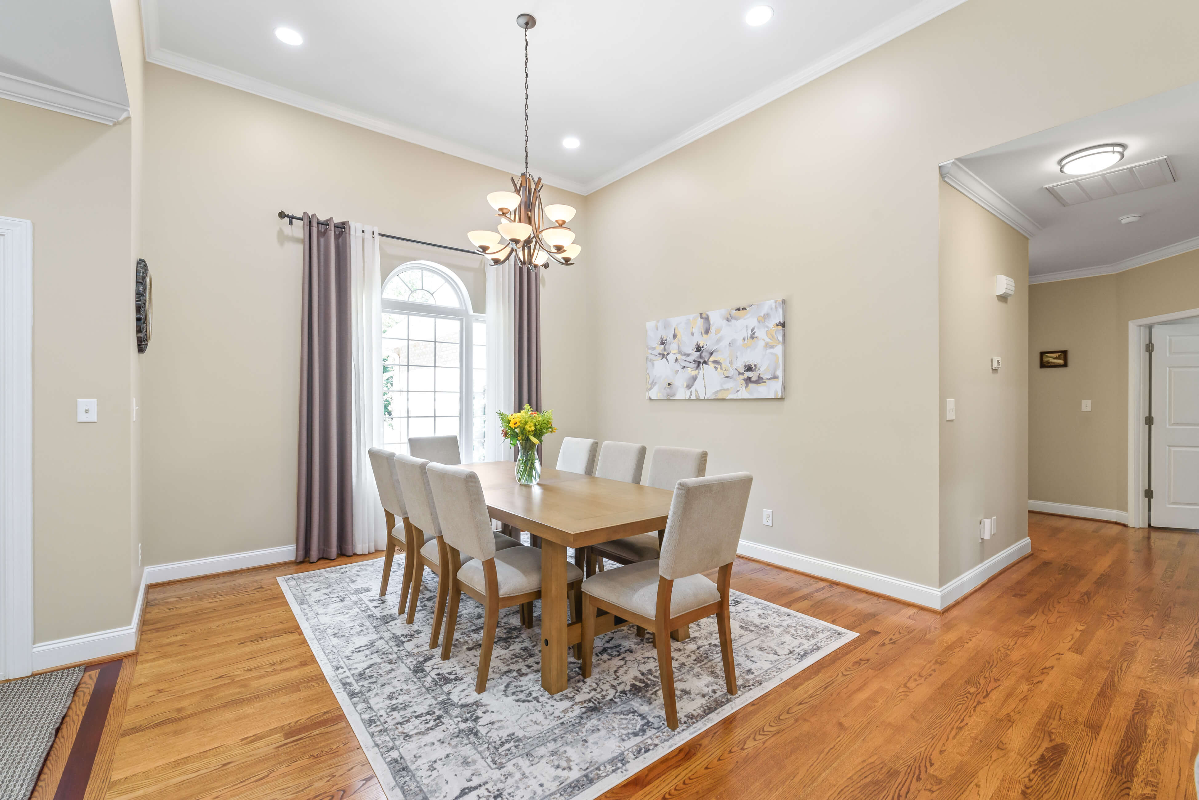 Dining room with chandelier, eight-seat table, area rug, and arched window with drapery