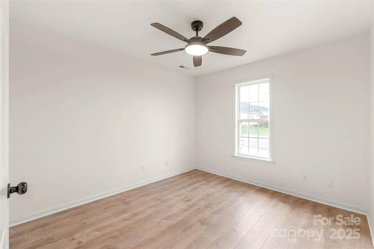 Bright bedroom with hardwood floors, ceiling fan with light, and single window.