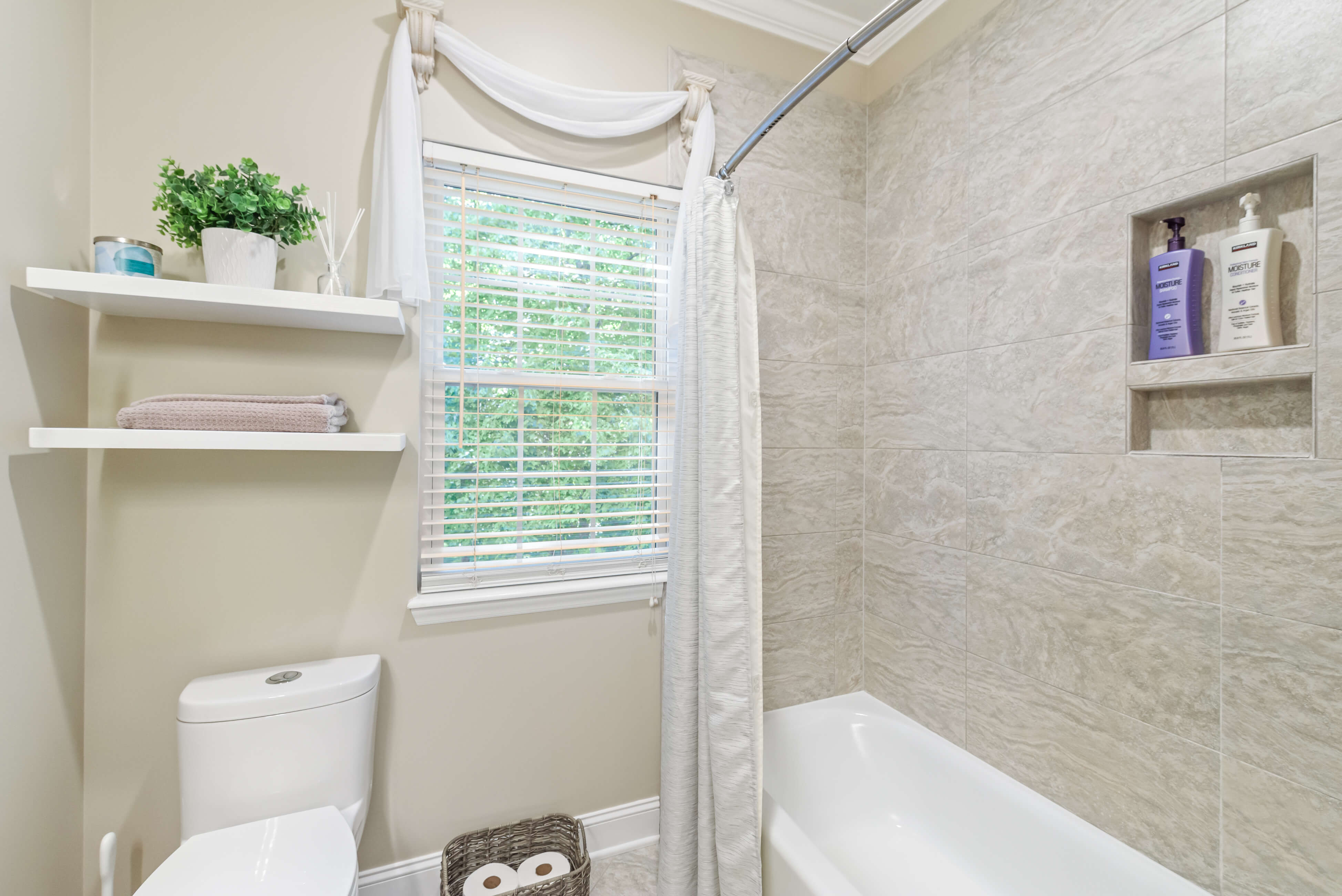 Tub‑shower with tile surround beside window, floating shelves, and toilet