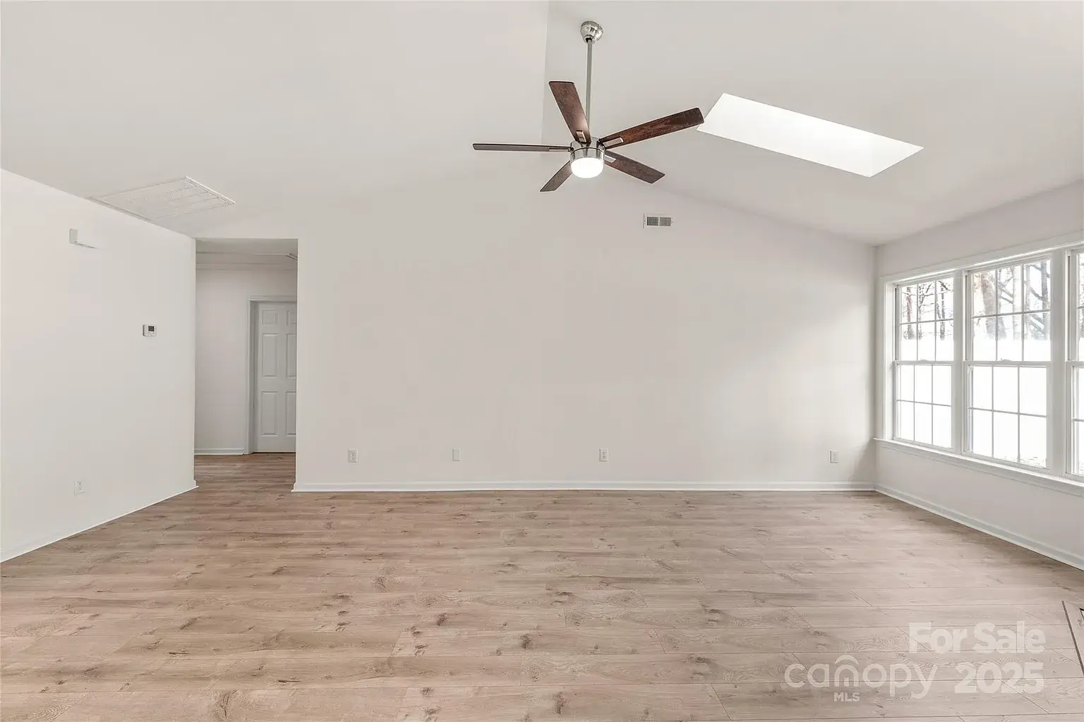 Open living area with vaulted ceiling, skylight, ceiling fan, large window, and wood flooring.