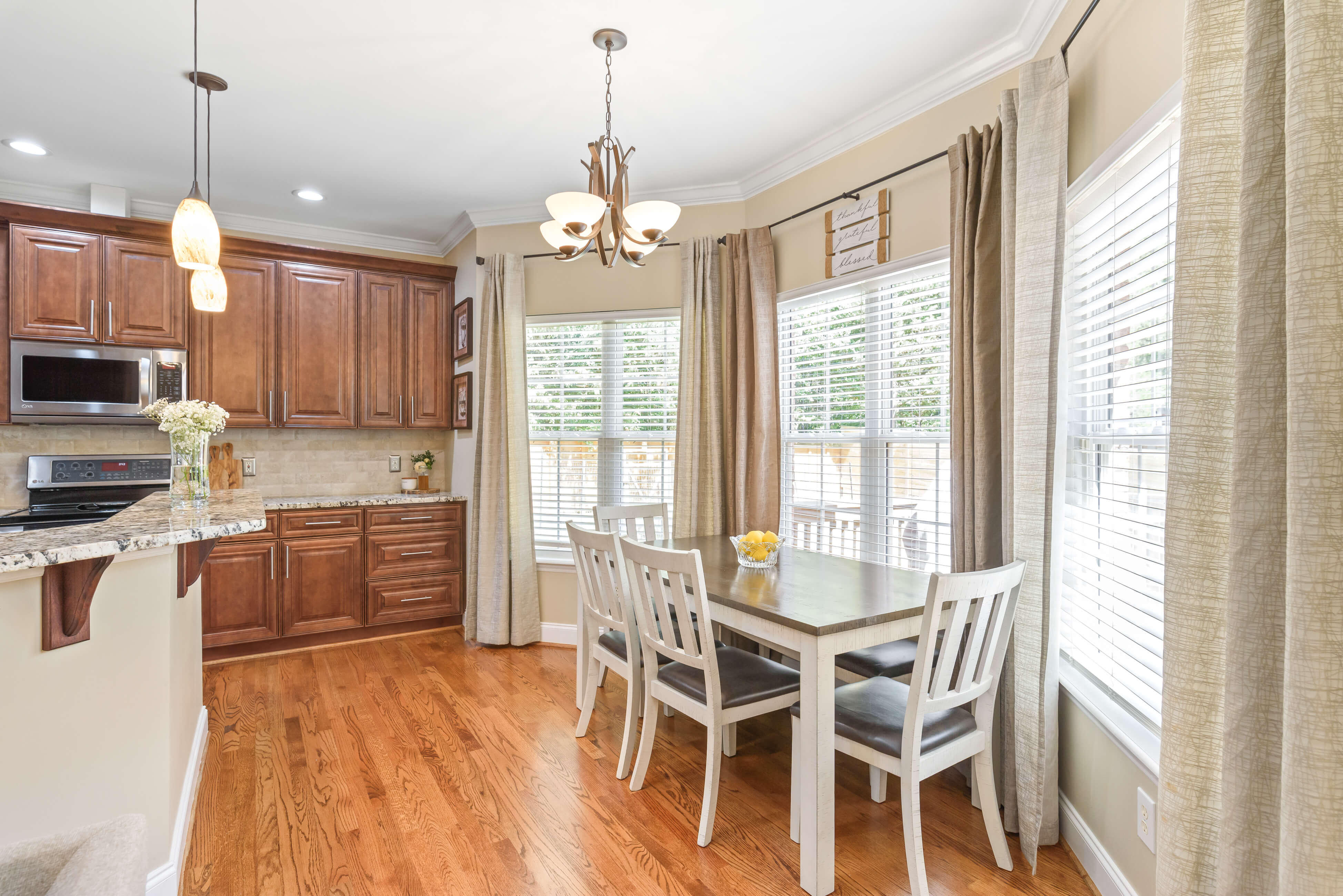 Breakfast nook with four‑seat table, bay windows, and drapery next to kitchen