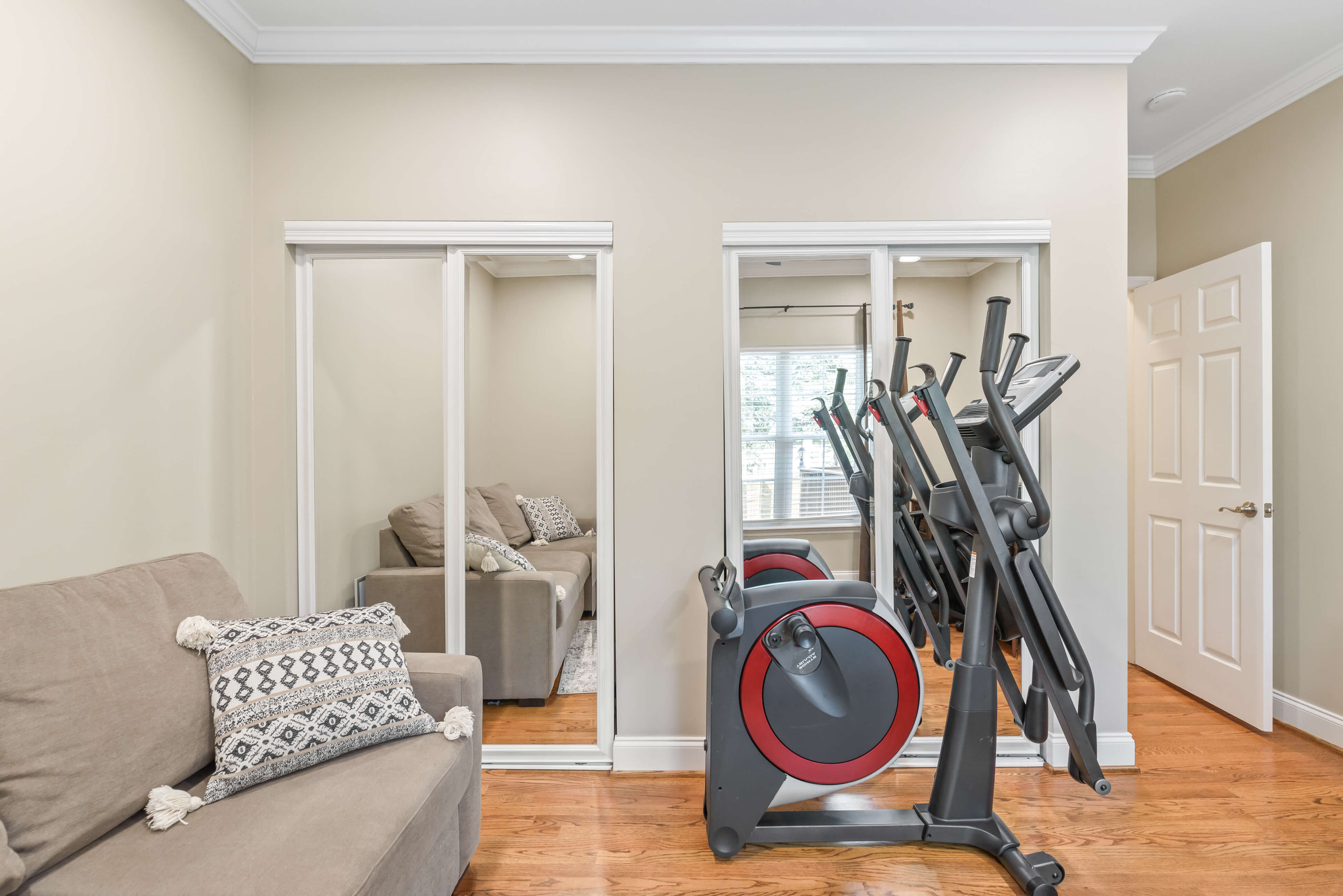 Home office with sofa, accent pillow, and exercise equipment beside mirrored closets