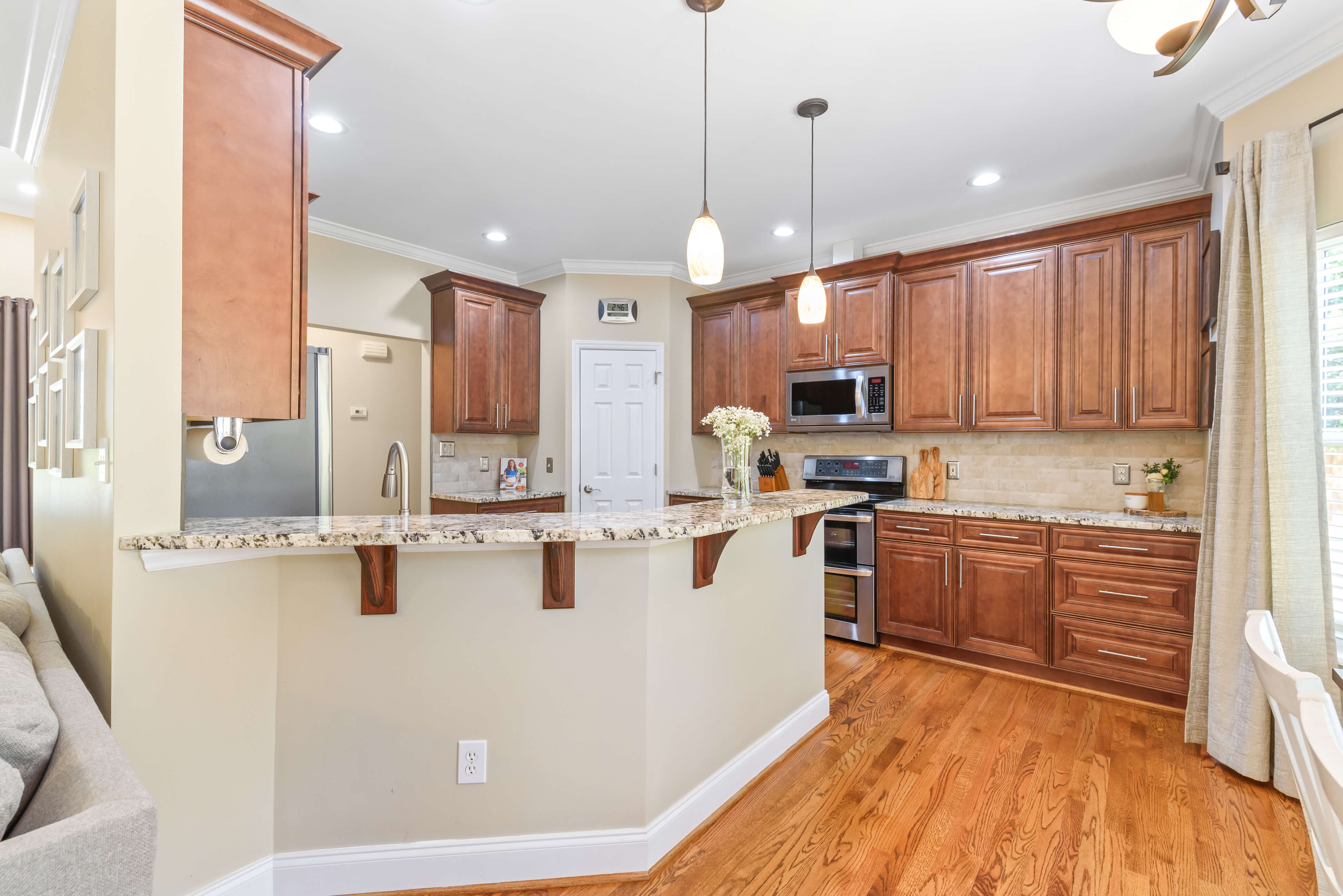 Kitchen with granite breakfast bar, pendant lighting, wood cabinetry, pantry door, and stainless appliances