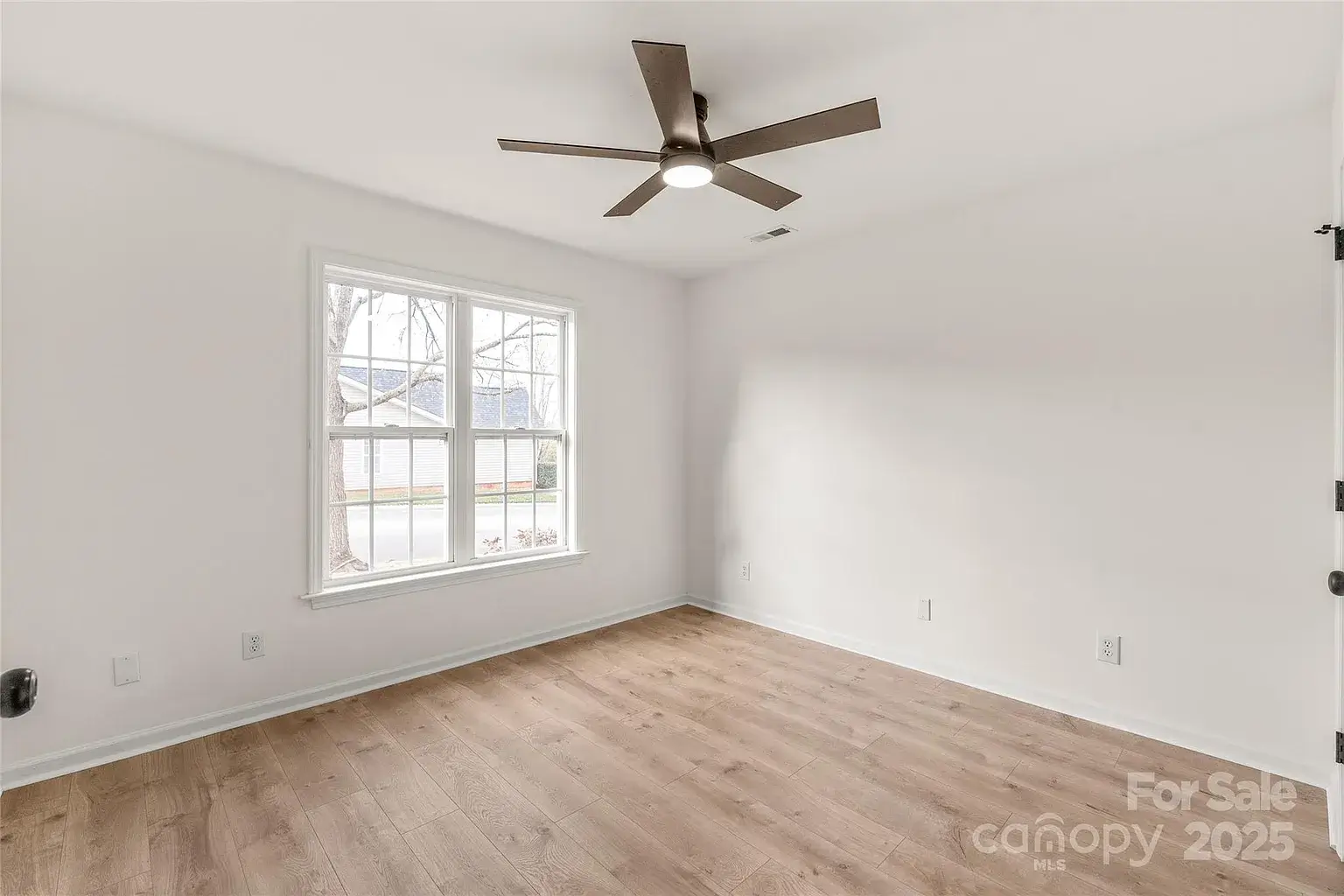 Empty bedroom with hardwood floors, white walls, ceiling fan with light, and double window.