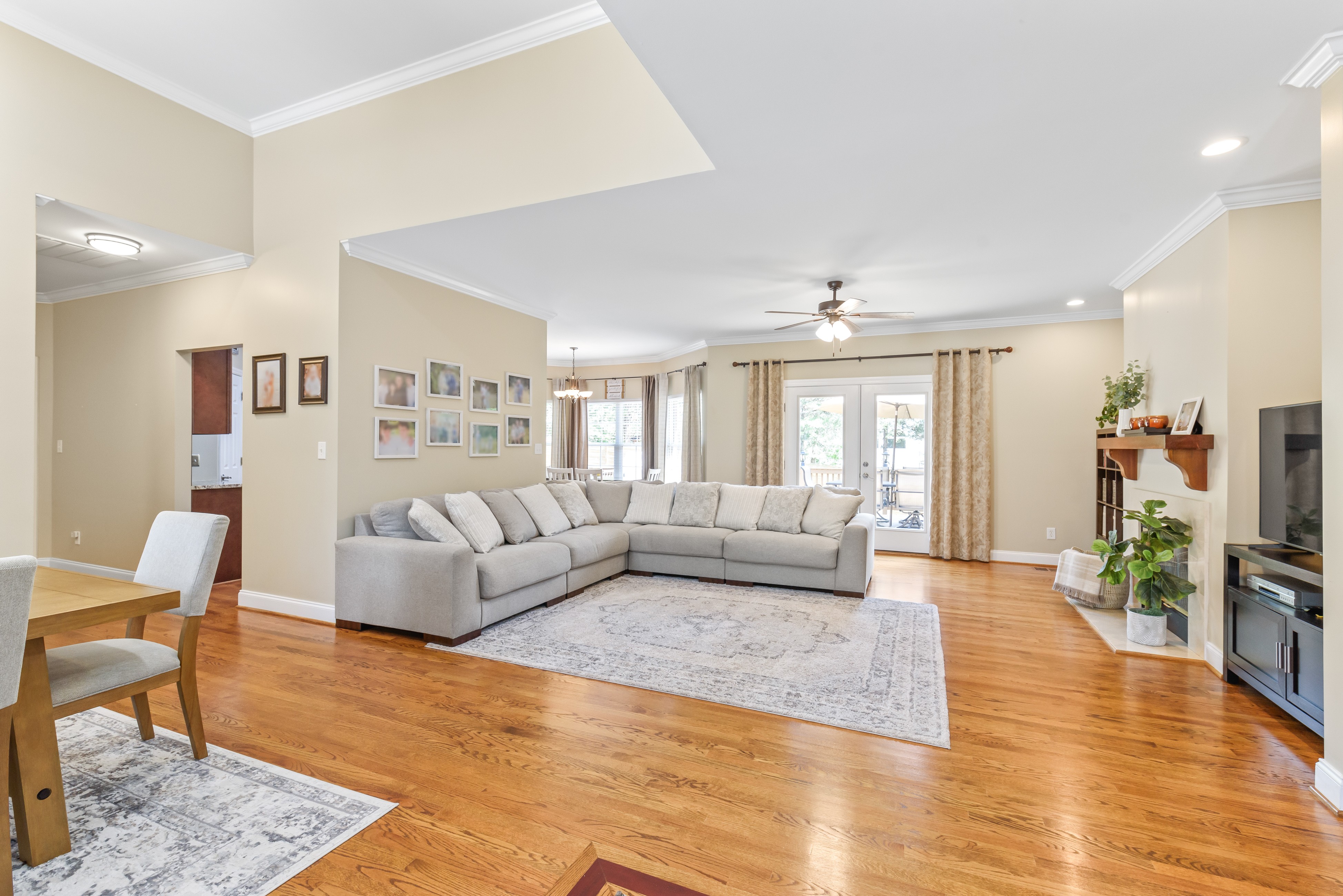 Open living room with hardwood floors, large sectional sofa, ceiling fan, and French doors to covered porch
