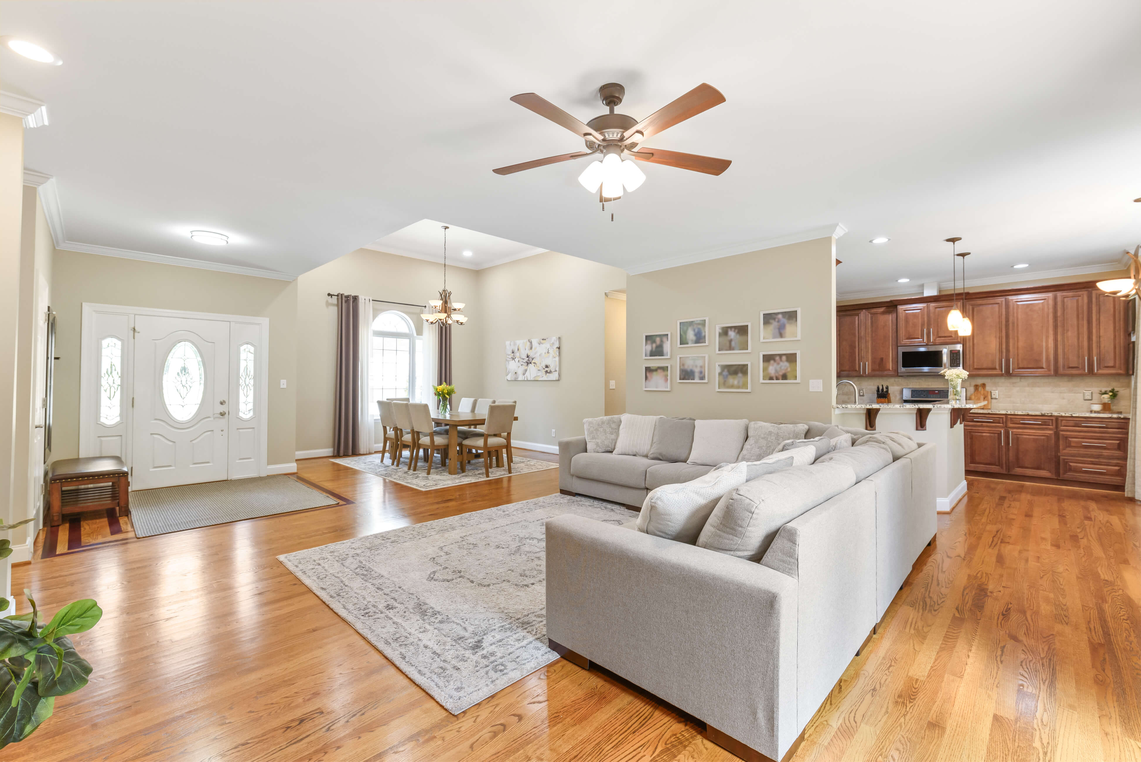 Open concept living, dining, and kitchen with hardwood floors, ceiling fan, and double front doors