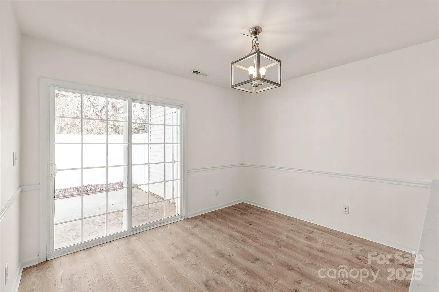 Dining area with modern pendant light, chair rail molding, wood flooring, and sliding glass door to patio.