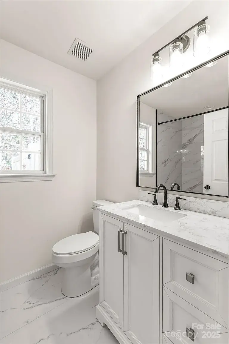 Bathroom with white vanity, marble countertop, black fixtures, large mirror, toilet, and window.