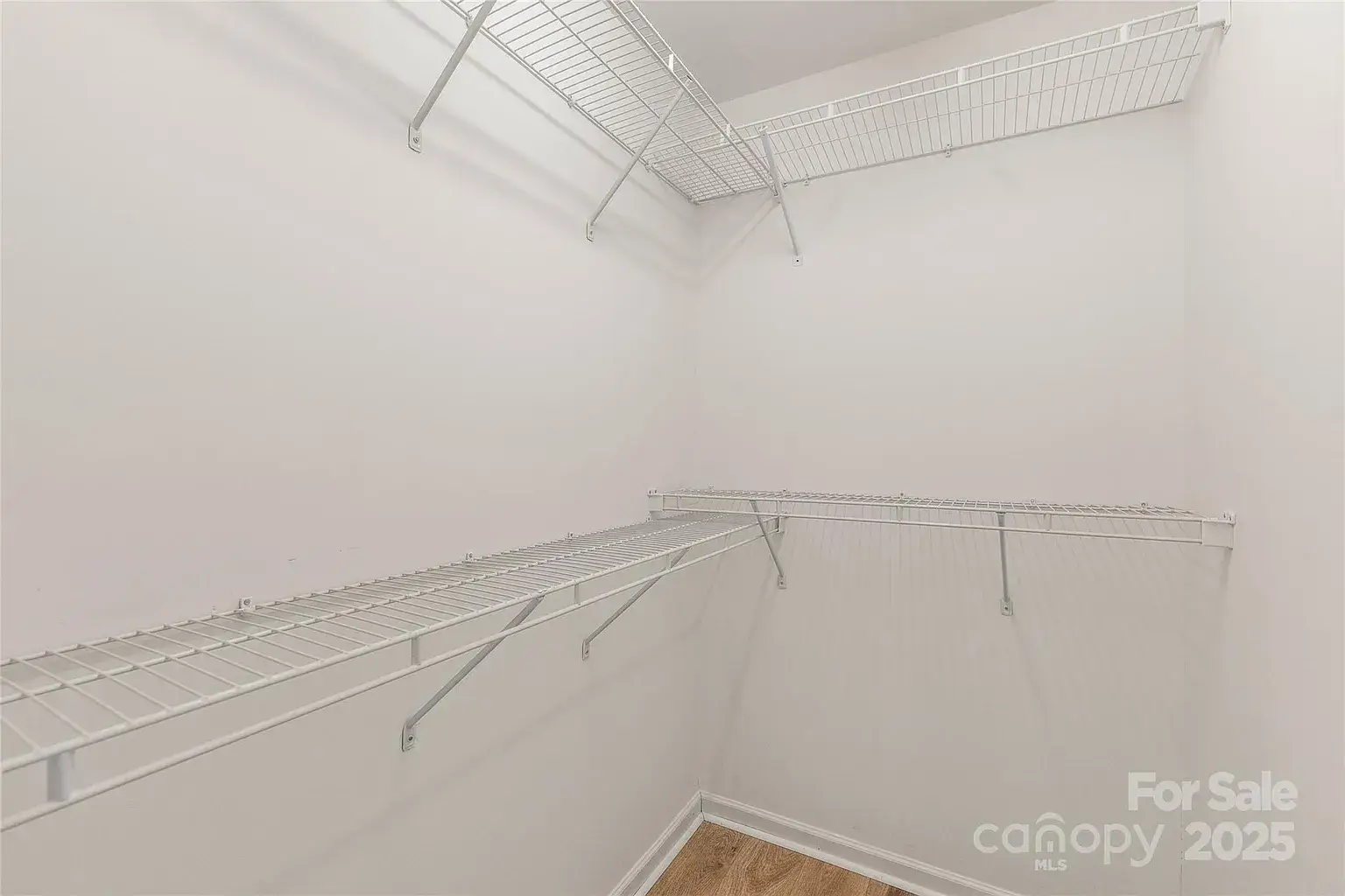 Walk-in closet with white walls, wood-look flooring, and wraparound wire shelving.