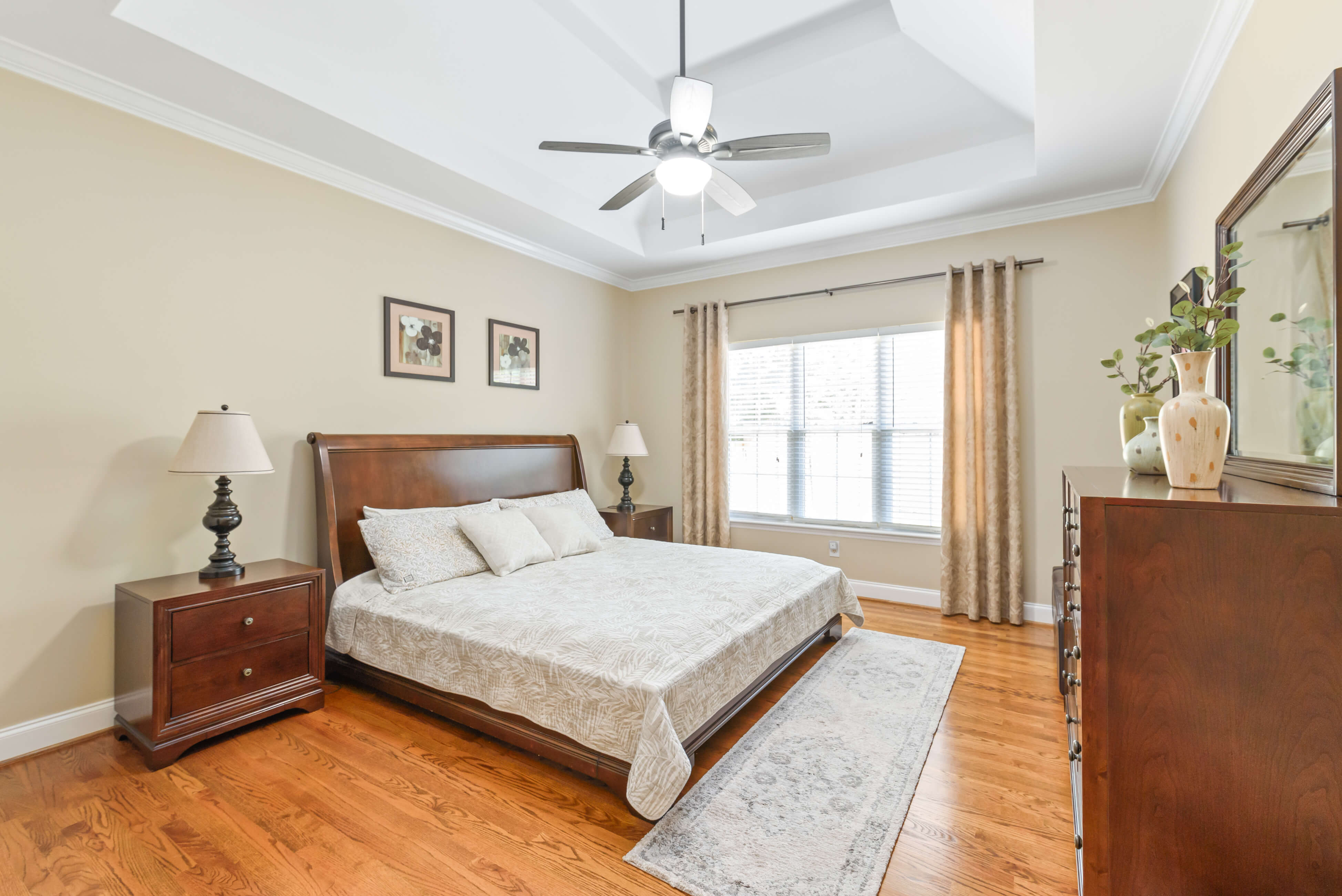 Primary bedroom with tray ceiling, ceiling fan, sleigh bed, and large window