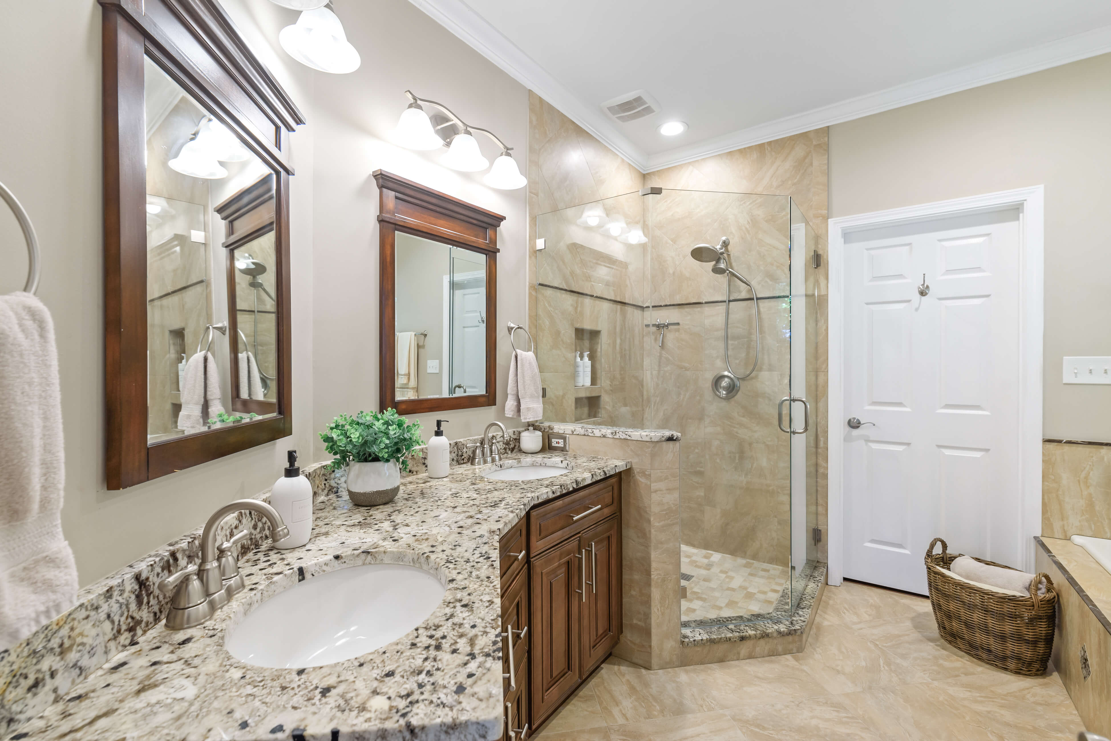 Primary bathroom with granite dual sinks, framed mirrors, and glass walk‑in shower