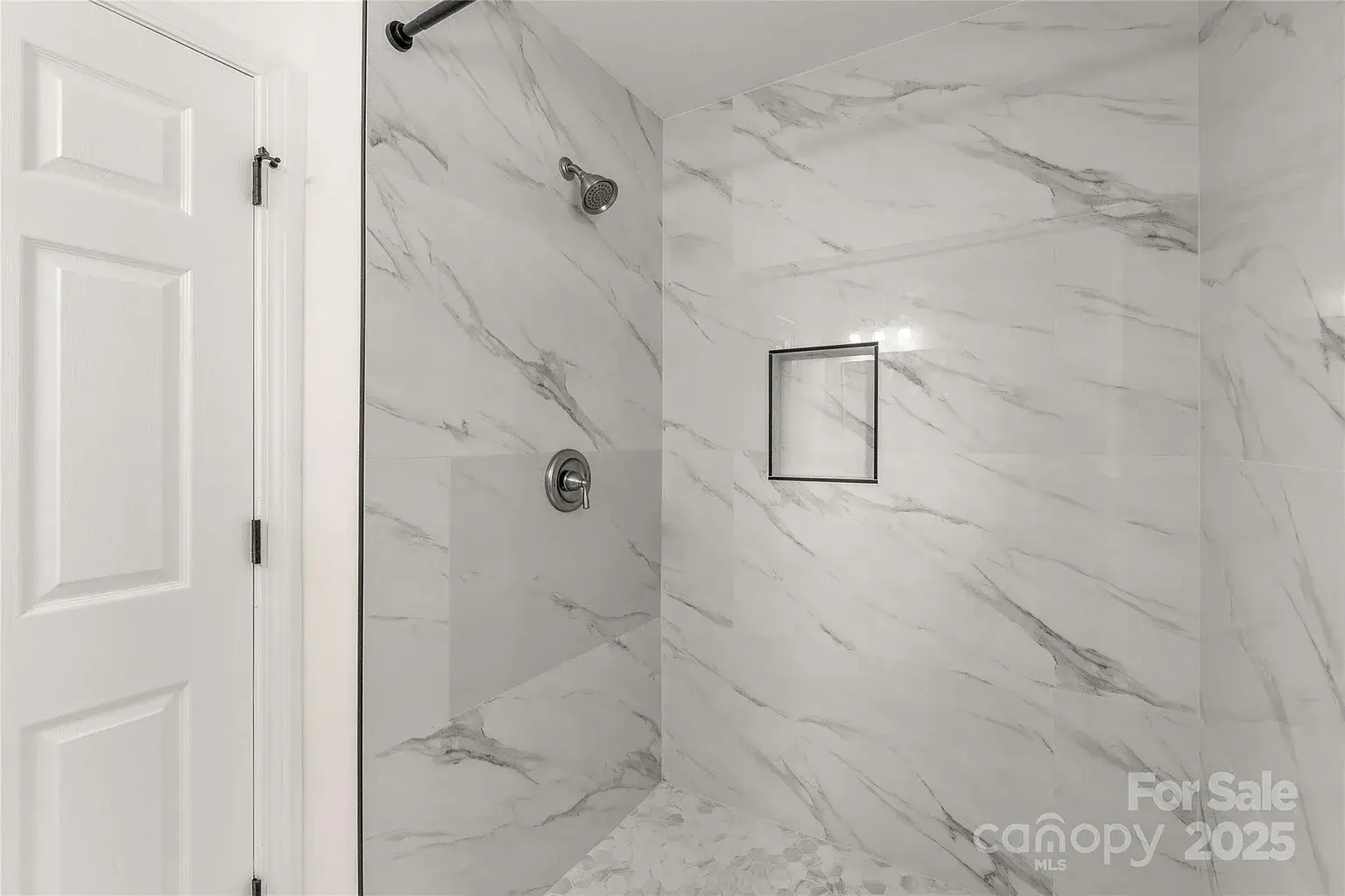Walk-in shower with marble-look tile walls, built-in niche, and chrome shower fixtures.