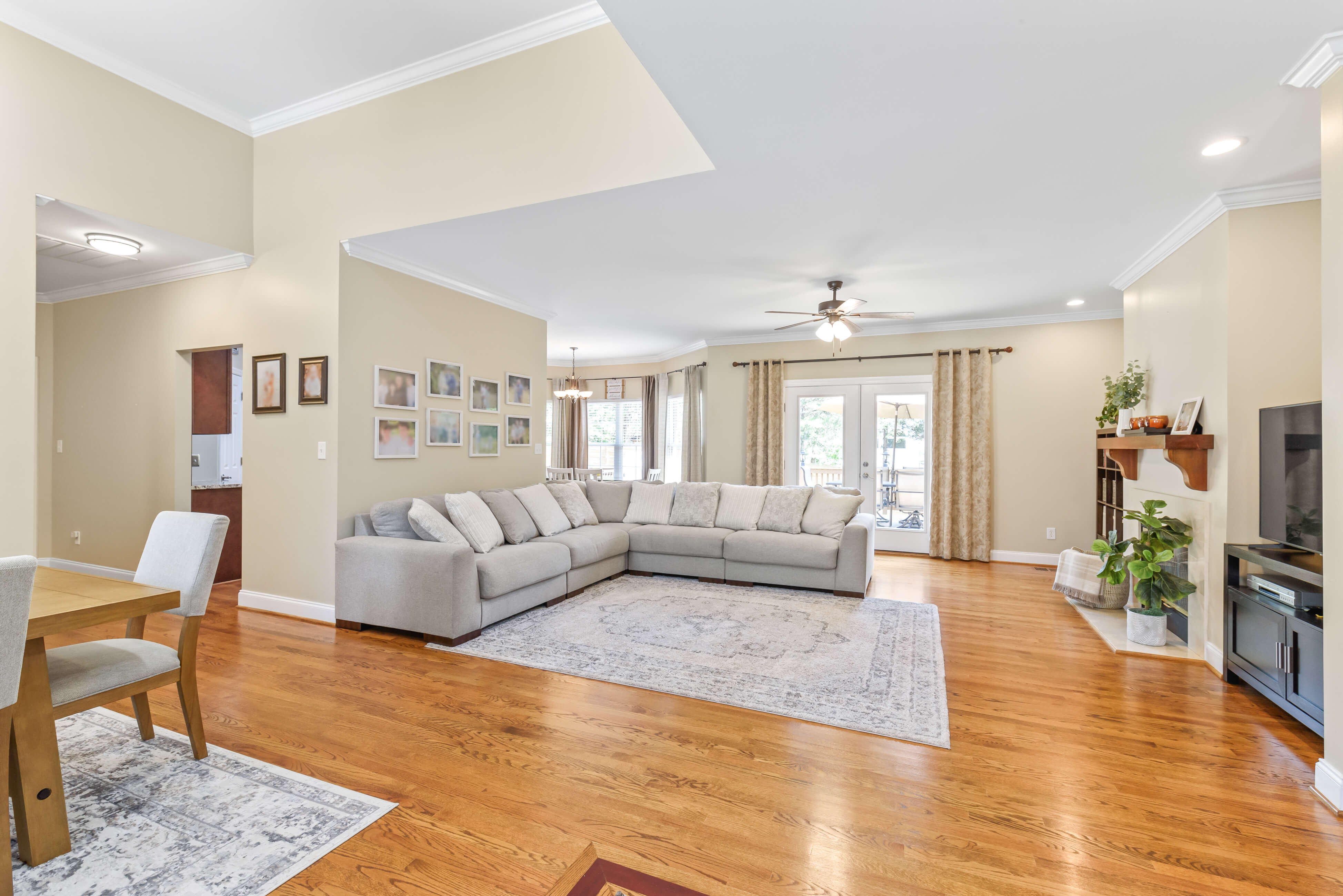 Open living room with hardwood floors, large sectional sofa, ceiling fan, and French doors to covered porch