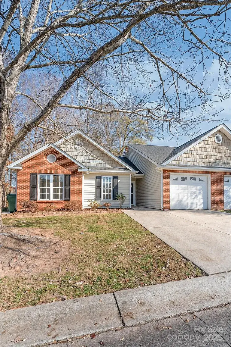 Front exterior of single-story brick and siding home with attached garage, driveway, and mature trees in Mount Holly, North Carolina.