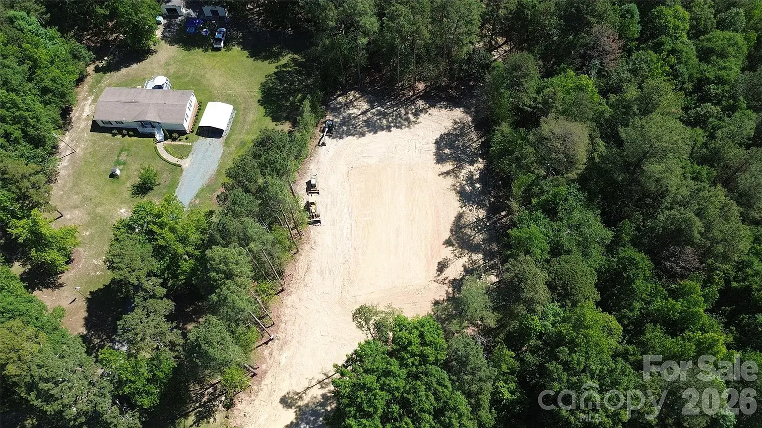 Aerial view of a cleared homesite on a wooded 2-acre lot in Monroe, North Carolina, surrounded by mature trees and neighboring properties.