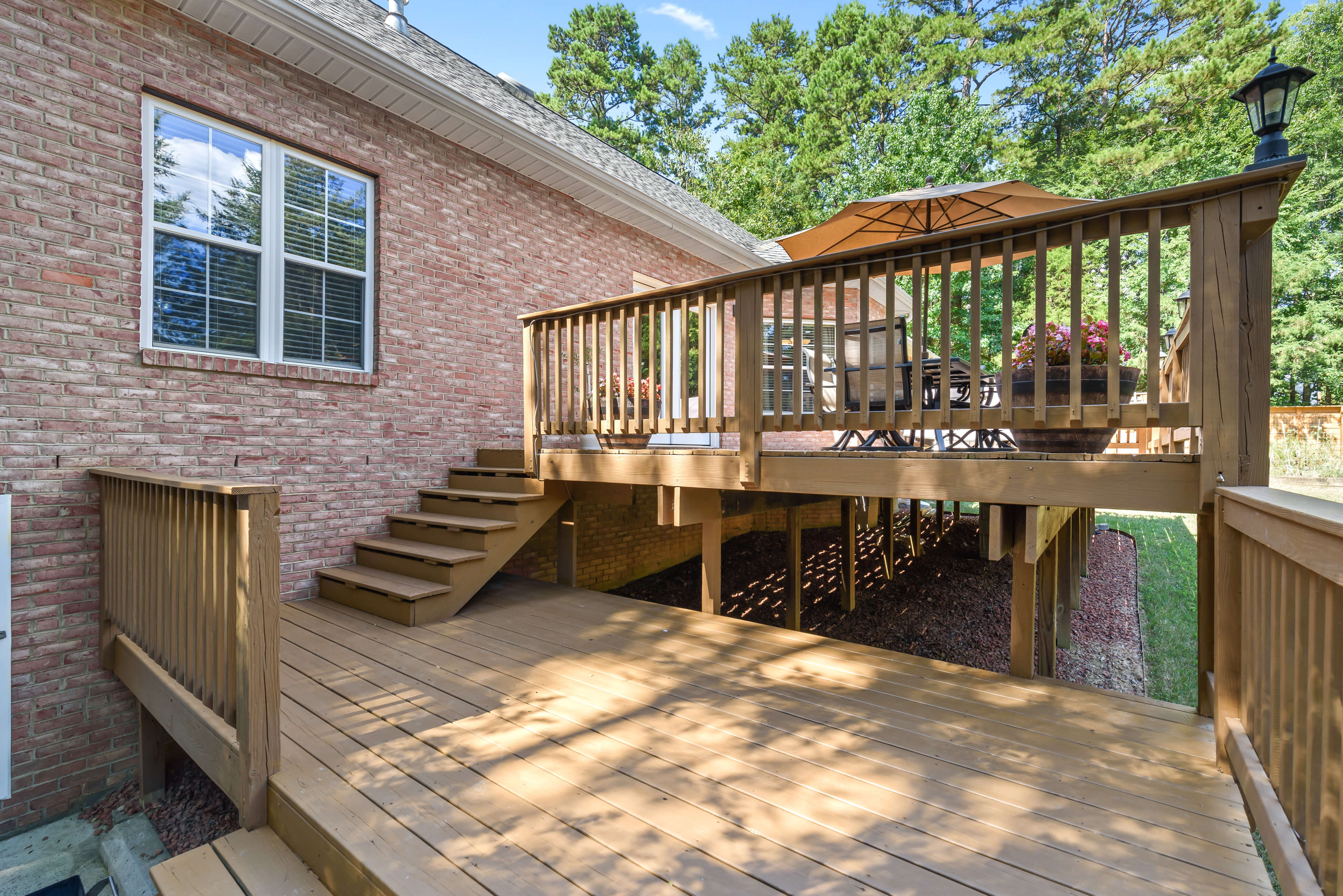 Multi‑level wood deck with steps and lower landing, raised railings, and shaded yard beneath.