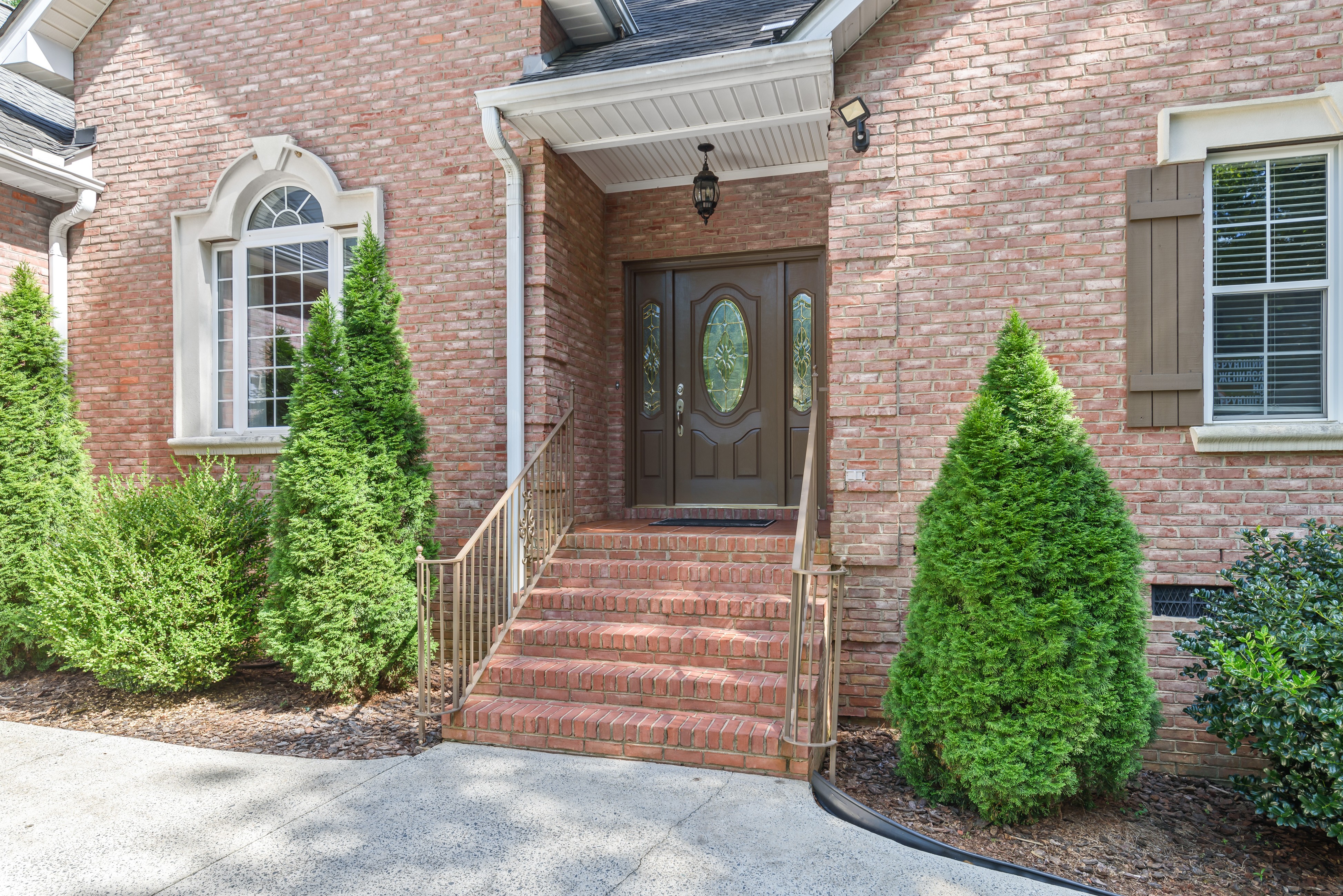 Front porch detail with double doors, brick steps, railings, and evergreen landscaping