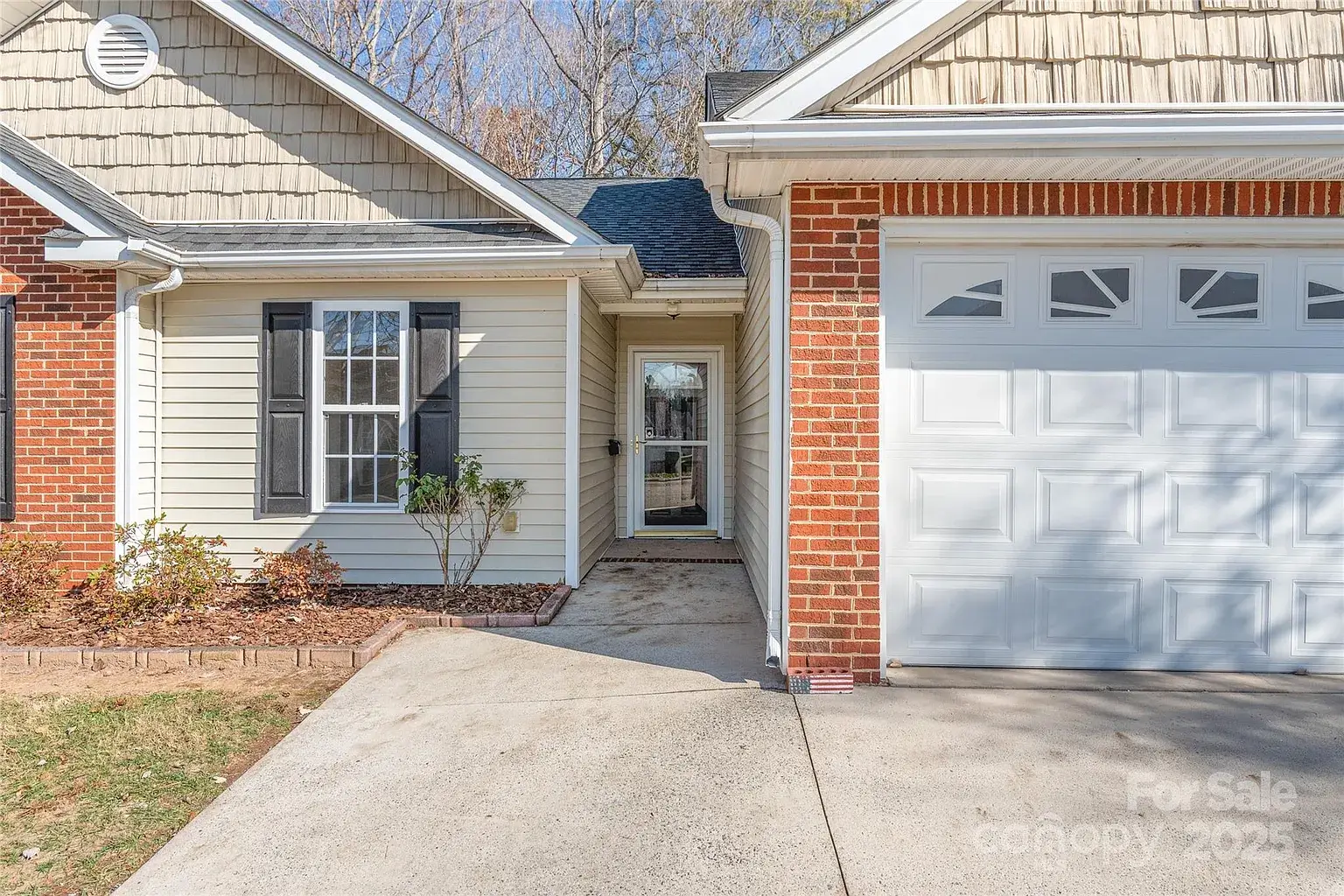 Front entry walkway and attached garage of a brick-and-siding home with covered entry and black shutters in Mount Holly, North Carolina.