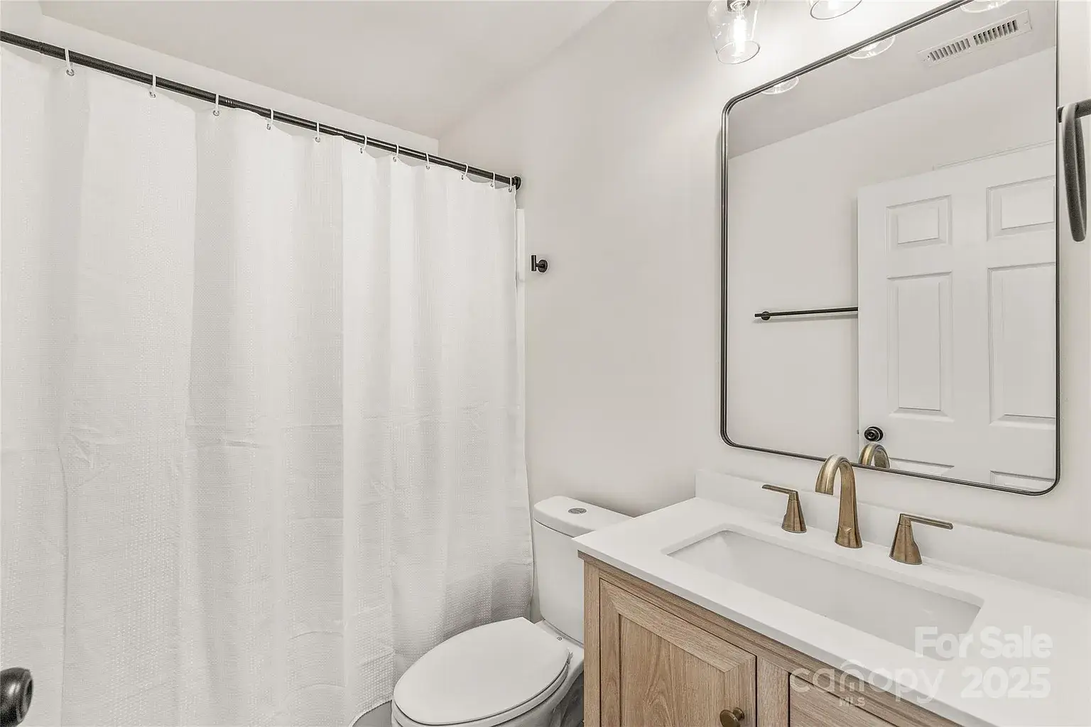 Full bathroom with white shower curtain, toilet, wood vanity with quartz countertop, and wall-mounted mirror.