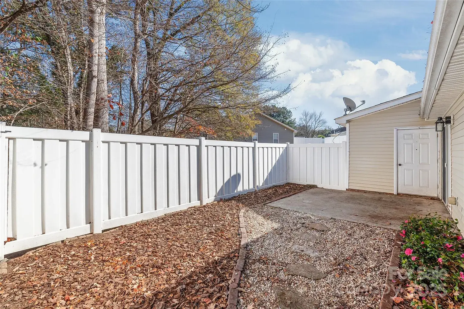 Fenced backyard with white vinyl privacy fence, gravel walkway, and concrete patio beside the home.