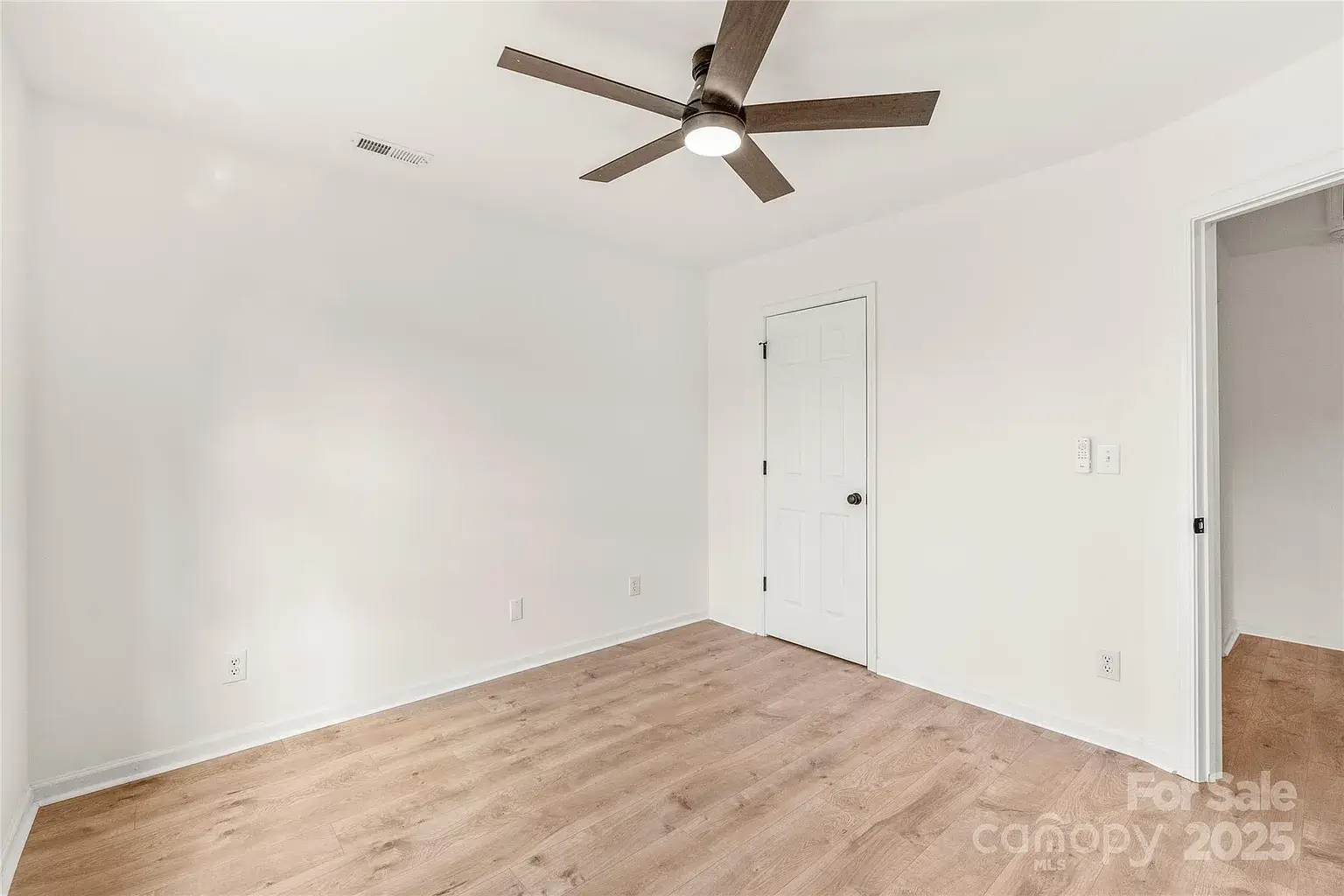 Empty bedroom with hardwood floors, white walls, ceiling fan with light, and single door.